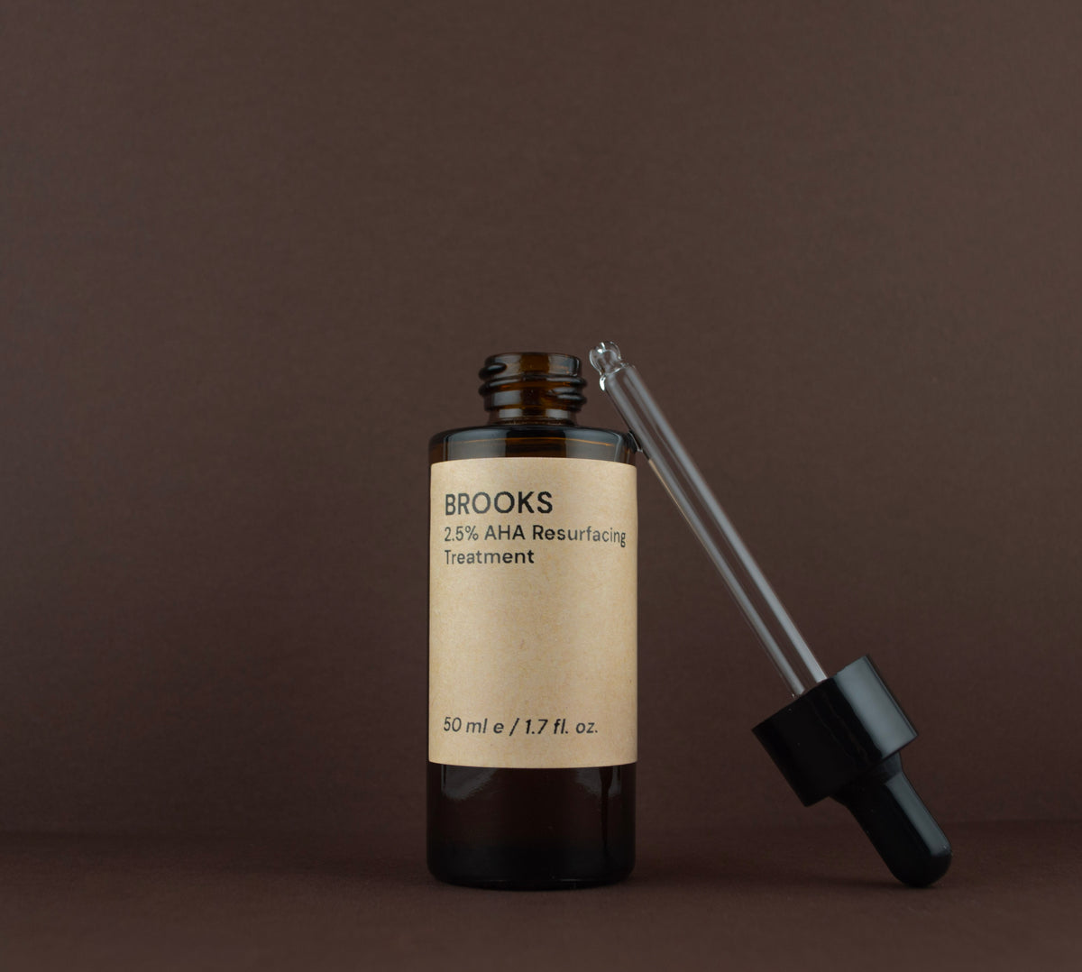 Open bottle of Brooks 2.5% AHA liquid exfoliant showing the glass dropper pipette resting on the rim.