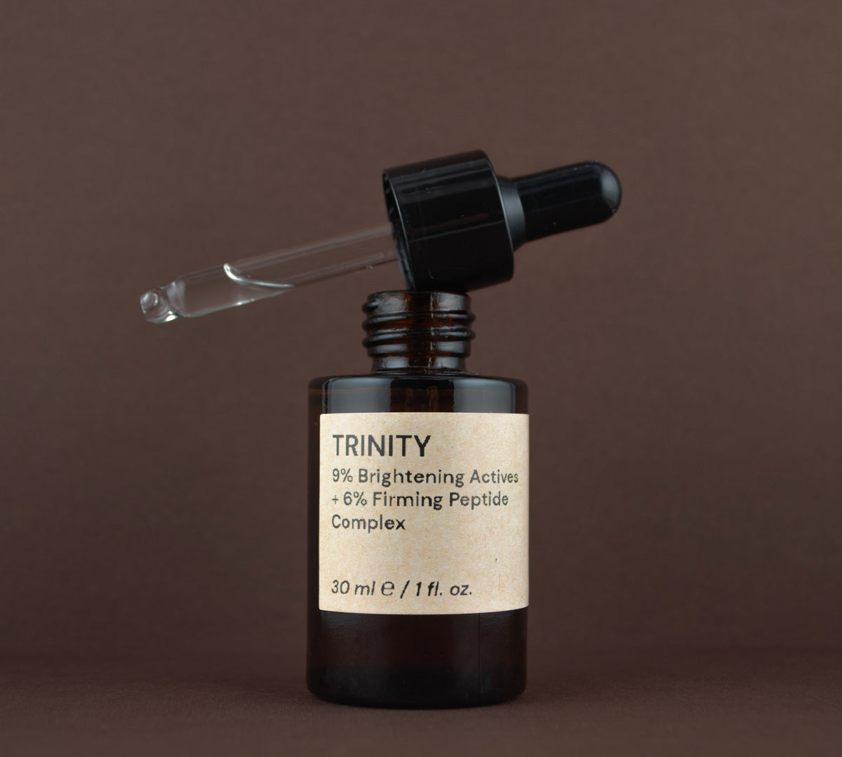 Open bottle of Trinity brightening and firming peptide complex showing the glass dropper pipette resting on the rim.